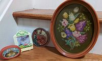 Group shot showing all four items: needlepoint, candle holder box, suncatcher, mini cat frame