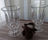 Front view of two pressed glass vases and ceramic fish tealight holder on surface