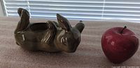Rabbit ceramic tealight holder lying on back next to red stone apple