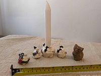 Group shot showing three black-and-white cat figurines, matching cat candle holder with taper, brown cat figurine, and measuring tape for scale