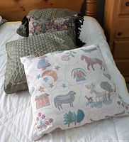 Front view showing pictorial tapestry pillow, one olive quilted pillow, floral tasselled pillow
