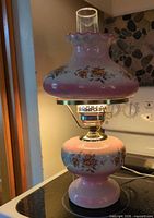 Full view of pink floral ceramic hurricane lamp on stove
