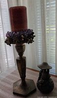 Brass candlestick with candle and beaded ring beside ceramic figurine