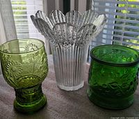 Group shot of three pressed glass pieces: clear ribbed vase center, green footed vase left, green cylindrical vase right