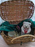 Basket open showing scarf, teacup, saucers and bear tin inside