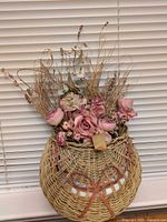 Front view of wicker wall basket showing woven bow detail and pink floral arrangement
