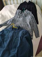 All three tops laid out: fleece jacket, cowl-neck sweater, black cardigan
