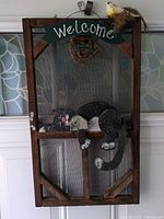 Front view of the wood screen door style hanger showing welcome sign, cat figure, bird nest and wreath