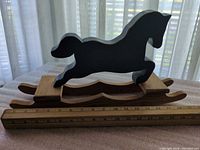 Side profile of blue wooden horse on natural wood base with ruler for scale