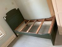 Full view of green painted wood single bed frame against wall