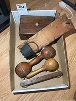 Lot overview in box showing wooden box, board with pot, two maracas, clacker