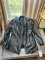 Full view of front of black leather jacket laid flat
