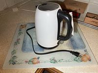 White electric kettle on glass board showing cord and plug