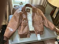 Full view of brown leather bomber jacket on plastic bin