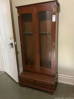 Front full view of tall wood bookcase cabinet with glass doors and lower drawers