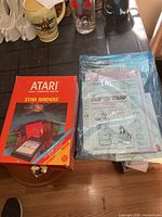 Front view of empty Atari Star Raiders box beside plastic sleeve containing several manuals