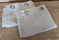 Both folded beige curtain panels with visible metal grommets