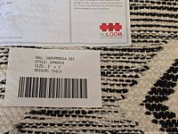Paper tag on rug showing SKU 200SPM001A-203, style SPM001A, size 2' x 3', origin India, atop rug pattern