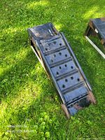 Full view of one metal car ramp on grass, showing perforated surface and extendable section