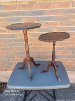 Two small wooden pedestal tables side by side on surface