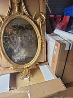 Front view of entire ornate oval gilt mirror in storage