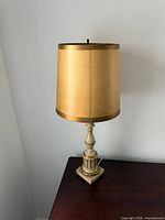 Front view of brass-tone vintage table lamp with gold drum shade on dark wood surface