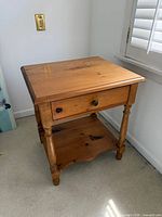 Front view of wooden side table showing drawer, turned legs, lower shelf