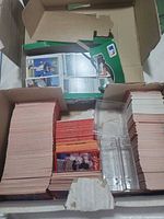 Open box showing two large stacks of baseball cards and partial green retail box lid