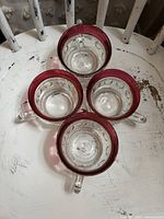 Top view of four handled punch cups showing clear thumbprint bodies and ruby flash rims