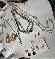 Overview showing five necklaces and three earring sets on chair