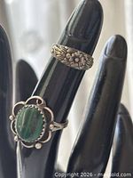 Front view of both rings on display hand showing malachite cabochon and floral band designs