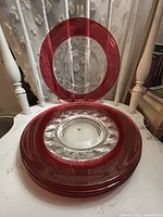 Stack of four clear glass plates showing ruby rims and thumbprint pattern