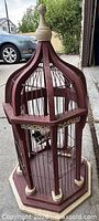 Front view of entire burgundy painted wood birdcage on driveway