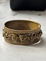 Side view of brass hinged bracelet showing repousse floral design