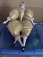 Full view of porcelain harlequin doll seated on container