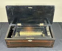 Music box open showing brass cylinder, glass cover, winding arbors