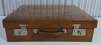 Closed brown leatherette suitcase showing front latches and handle