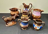 Group shot of seven copper lustre pitchers and cow creamer
