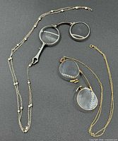 Silver and gold folding lorgnettes with chains displayed side by side