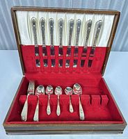 Open wood case displaying knives in lid and other pieces in tray
