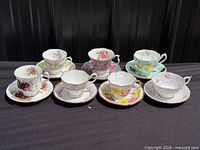 Front view of seven cup-and-saucer sets showing patterns and colours