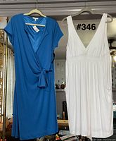 Front view of both dresses hanging: blue wrap and white sleeveless
