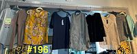 Eight tops and sweaters hanging on rack, showing variety and tags