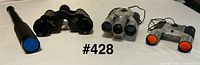 Four optical items laid out: black binoculars, silver camera-binoculars, compact binoculars, and collapsible telescope