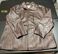 Front view of brown leather jacket laid flat, sleeves crossed
