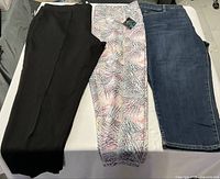 Three pairs of pants laid flat: black, multicolor, blue denim