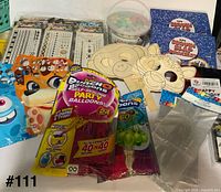Assorted sealed party favor items spread out including tattoo packs, chalk, slap bracelets, balloons, loot bags, wooden masks