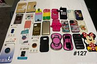 All phone accessories laid out: screen protector boxes and packs, packaged grips and wallet on left; array of loose phone covers on right