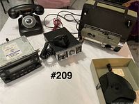 Group shot of all items: projector, CB radio with mic, car CD player, rotary phone, reel box