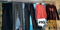 Five Under Armour garments hanging: three sweatpants and two hoodies